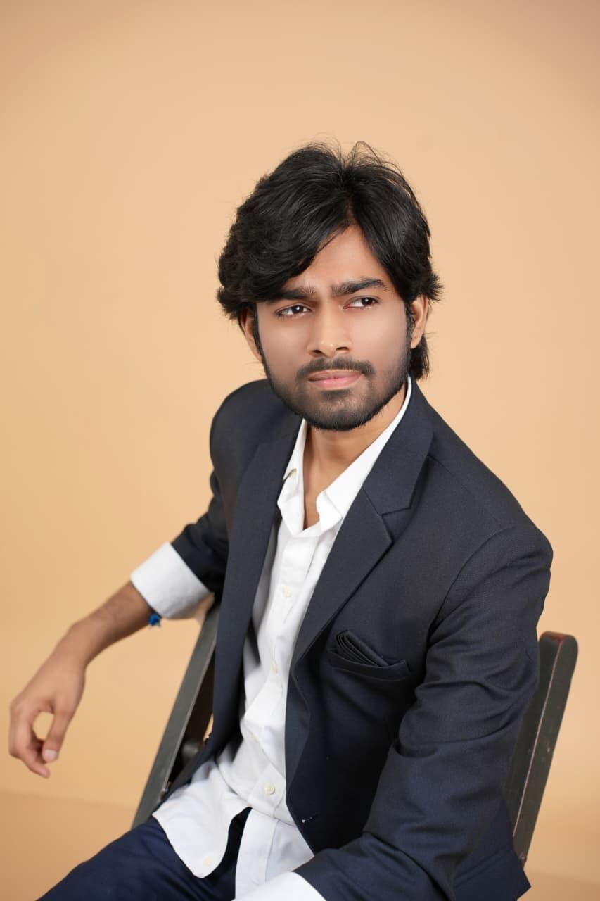 Seated on a chair in a blazer, arm resting back